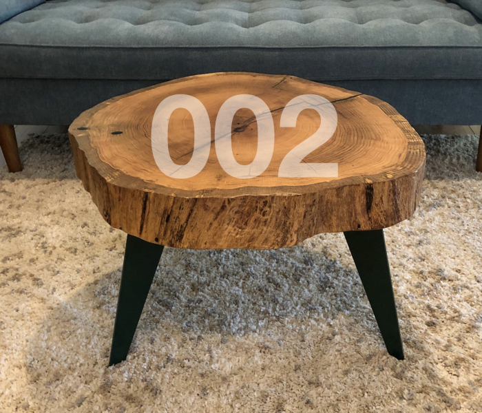 002 Image of a coffee table in perspective. The table has three thin aluminum legs in dark green color. The table top is a solid live edge slice of oak wood with natural finish. 